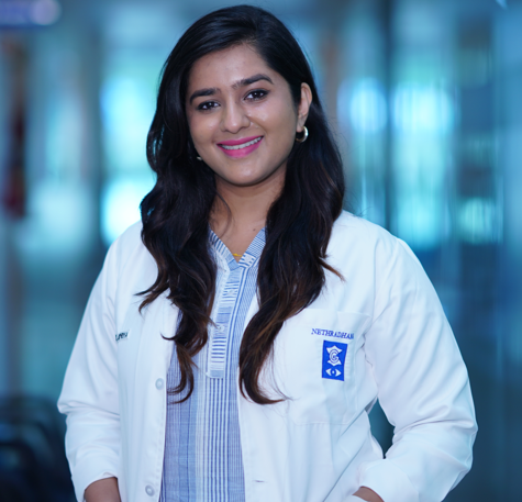 Female doctor in a white coat smiling in a bright hospital hallway, portrait-style.